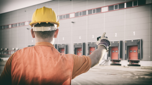 Homme portant un casque de sécurité montrant du doigt les quais de chargement et déchargement d'un entrepôt